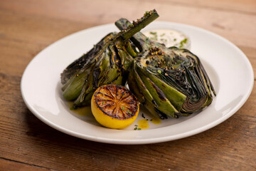 Grilled artichokes. Artichokes roasted in olive oil, topped with cheese sauce, garnished with scallions and parsley served in cast iron skillet. Classic American restaurant or French bistro side dish.