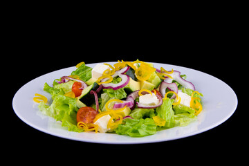 Salad with avocado and feta cheese - avocado, cucumber, feta, bell pepper, cherry tomatoes, lettuce. Closeup on a white plate on black background