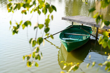 A small green boat with oars moored at the lake pier