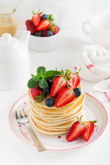 Sweet homemade stack of pancakes with pouring honey, fresh strawberry, mint in modern plate on light background. Space for text.