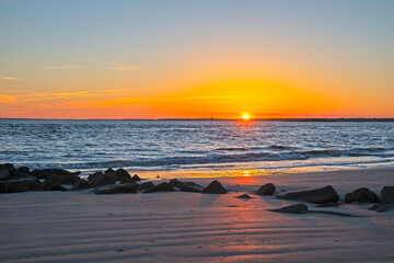 sunset on the beach at Sullivan's Island, SC, with orange glow in sky and rocks in foreground.