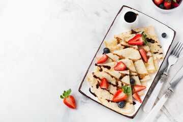 Thin crepes pancakes with chocolate sauce and fresh strawberry, top view.