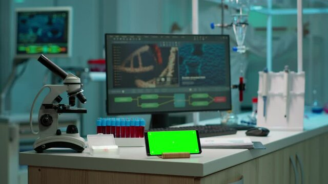 Scientist standing at monitor in background analysing virus evolution while phone with mock-up green screen working in front. Woman lab researcher examining vaccine developent bringing blood samples