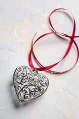 Fototapeta na wymiar Saint Valentine day greeting card, beautiful silver heart with red ribbon on grey texture