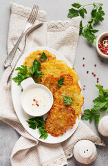 Potato pancakes with sour cream, herbs and garlic in white ceramic plate on gray old concrete background.