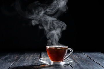 A hot cup of hot tea with steam with saucers placed on an old wooden table on black background...