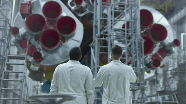 Two scientist engineers inspect the spacecraft, write on the tablet. A space rocket in a military hangar being prepared for launch. Space technologies. Construction of Big Rocket. Humanity in Space