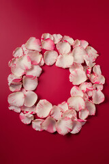Holiday round wreath made from light rose petals on red background