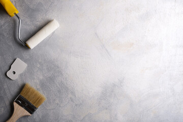 Spatulas for application of putty and brushes and rollers for painting on a gray concrete background.Top view