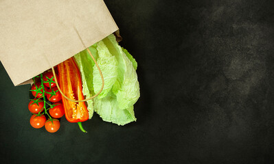 Lettuce leaves, red pepper, cherry tomatoes in a craft bag on a black background.