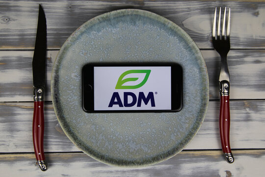 Viersen, Germany - May 9. 2020: Closeup of mobile phone on plate and wood table, cutlery with logo lettering of archer daniels midland adm food company (focus on center)