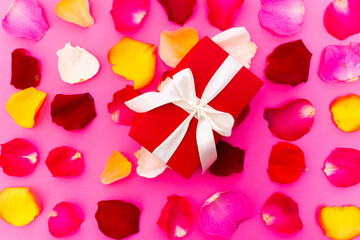 pink bright background with colored rose petals and a red gift box with a bow in the center valentines day discounts promotion