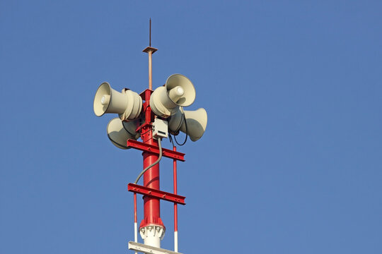 Tannoy megaphone system on a red pole against a blank blue sky background. Public Pa address.