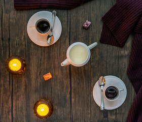 Top view of a two-person set of espresso coffee with white cups and milk jug with yellow candles on wooden background