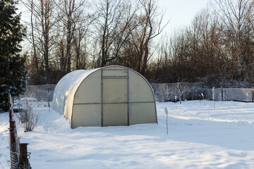 Greenhouse in the vegetable garden in winter. Small greenhouse with a metal frame covered with polycarbonate.