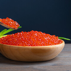 Red caviar in a wooden cup on a wooden background with a spoon.