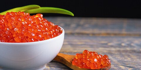Red caviar in a wooden cup on a wooden background with a spoon.