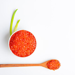 Red caviar in a wooden cup on a white background with a spoon.