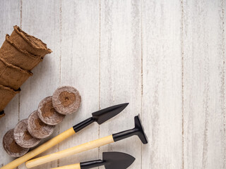 Gardening at home. Tools, peat pots and pressed ground for seedlings. Flatlay on white wooden background.
