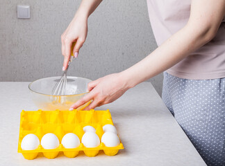 A woman in the kitchen holds a whisk in her hands with a yellow handle and whips them with eggs in...