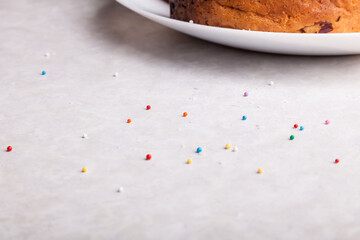 Close-up of confetti balls scattered on the table in red, yellow, blue, green - a traditional confectionery decoration against the background of baked Easter cakes on a plate.