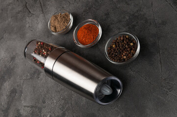 Electric spice mill. Lies on the table. Nearby are cups of spices. Grey background.