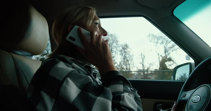 Distracted middle-aged woman talking on phone while driving car, unsafe driving