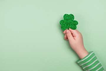 Little child holding shiny green Clover. St Patricks Day. Top view, flat lay, copy space
