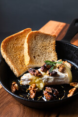 Food concept spot focus homemade Baked Brie cheese with honey and walnuts in skillet iron pan on wooden board with black slate stone copy space
