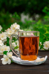 Glass cup with tea among flowering bushes jasmine. Outdoor, picnic, brunch. Green leaves background in blur.