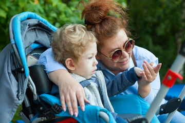 Mother with disabled son walking outdoors with walker, medical mobility equipment.