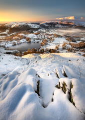 Snow on mountains above Loughrigg Tarn on a cold Winter morning with beautiful golden light. Breathtaking English countryside scene. Lake District, UK.