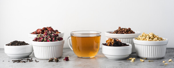 Glass tea cup and Different types of tea in bowl on white background. Rose hips, jasmine, rose flower, green, berry, hibiscus tea