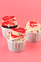 .Cupcake. Cupcakes in the shape of a heart in white cups with inscriptions: love,  happy on a pink background. Valentine's Day. Vertical photo