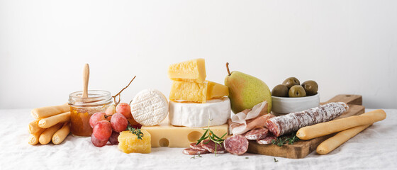 Cheese, sausage, ham, fruits, jam and grissini bread sticks on the table. Light background,...