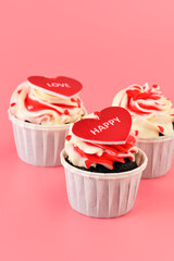 Cupcake. Cupcakes in the shape of a heart in white cups with inscriptions: love,  happy on a pink background. Valentine's Day. Vertical photo