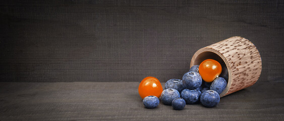Fototapeta na wymiar blueberry berries in a wooden barrel with physalis berries on a wooden background