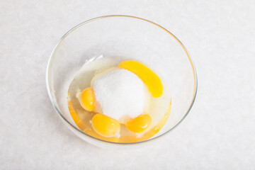 Four yellow yolks with egg protein and sugar in a deep plate  before cooking on a white isolated background.