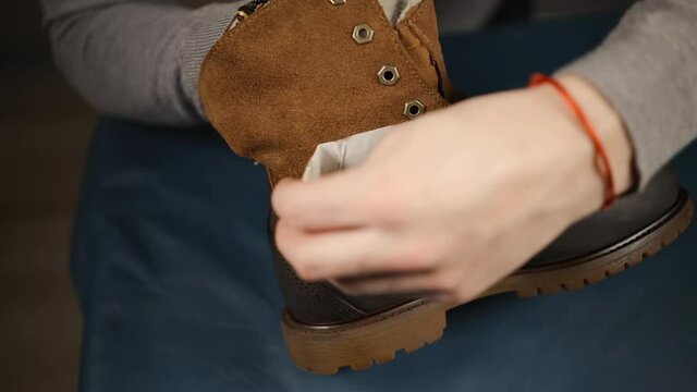 Side view: Male cobbler showing repaired boots during process of restoration at home or at workshop
