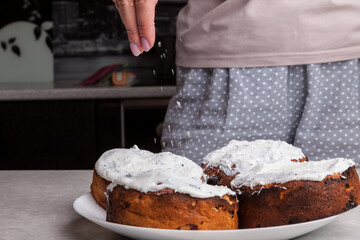Close-up of Easter cakes on a plate and female hands with manicure sprinkling multicolored confetti on white glaze - a traditional decoration for the Christian holiday.