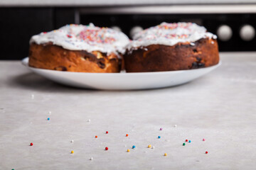 Close-up of confetti balls scattered on the table in red, yellow, blue, green - a traditional confectionery decoration against the background of baked Easter cakes on a plate.