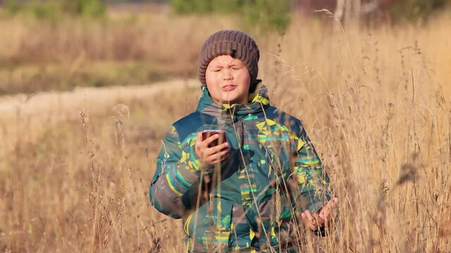 Close-up of a boy in the tall grass, he is talking on the phone online. Walk in the park in autumn. Camping on a hike. Healthy lifestyle concept. At sunset, in the evening, warm soft light.
