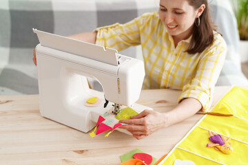 happy smiling woman sewed children's applications from felt, on sewing machine.