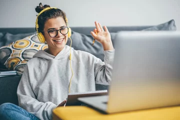 Foto op Plexiglas Millennial woman having video call on her computer at home. Smiling girl studying online with teacher. © Mariia Korneeva