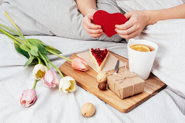 The girl is holding a red heart. Congratulations on Valentine's Day on February 14. Breakfast in bed and a gift