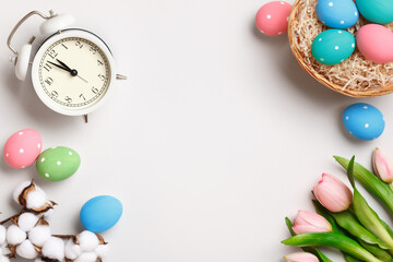 Fototapeta na wymiar Happy easter. Multicolored eggs, tulips and an alarm clock on a light gray background. Flat lay greeting card invitations with copy space.