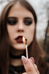 The girl has a burning match in her hand. The hearth is burning. In the frame of the face of a young beauty with dark gothic makeup.