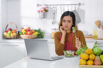 Displeased young Asian woman eating salad . unsatisfied woman eating vegetarian food  while using...