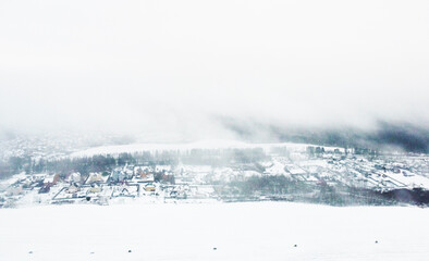 Top view of snow-covered houses in suburb near fields in winter
