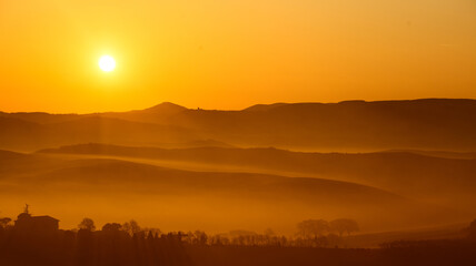 warm dawn sun on misty rolling hills in the tuscany countryside